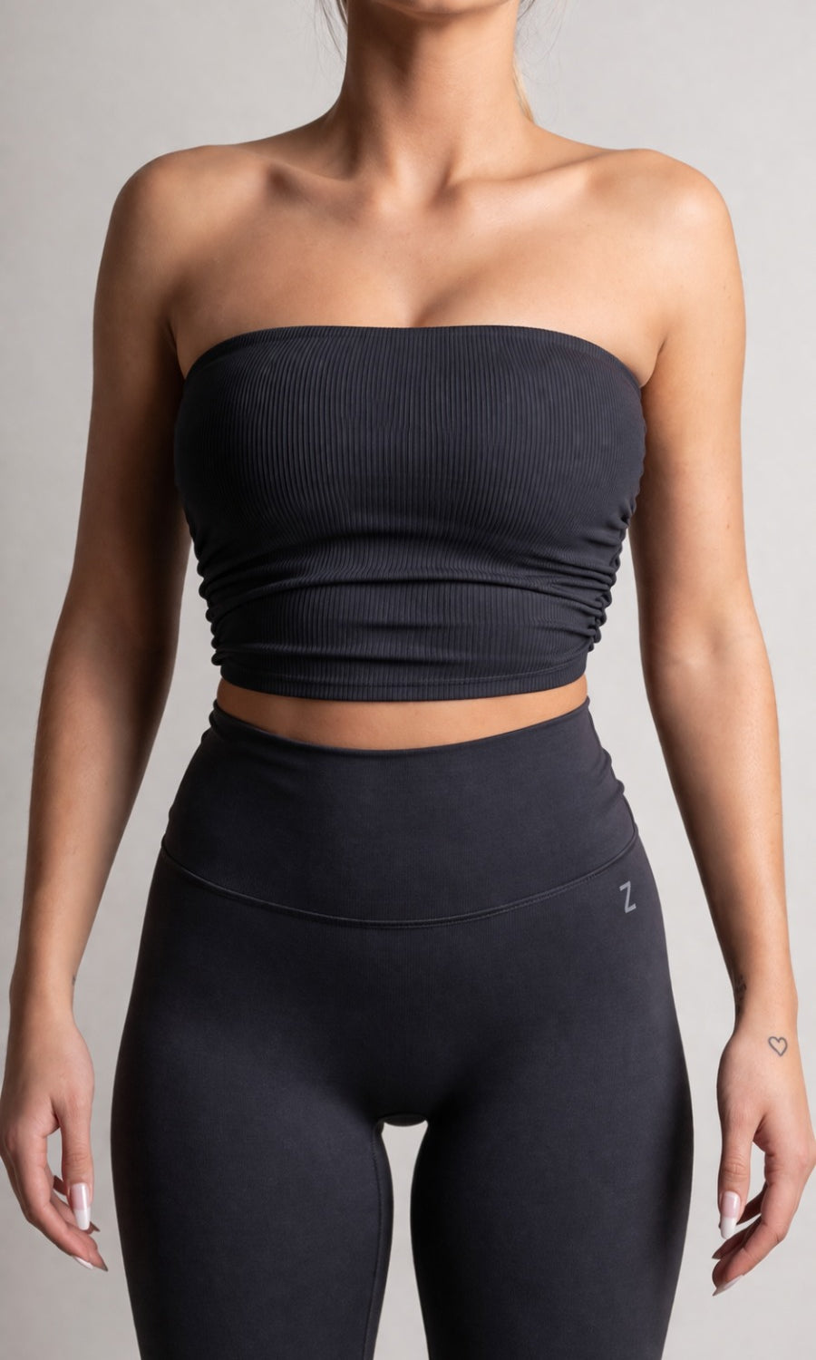 Person wearing a black strapless top and high-waisted leggings on a gray background