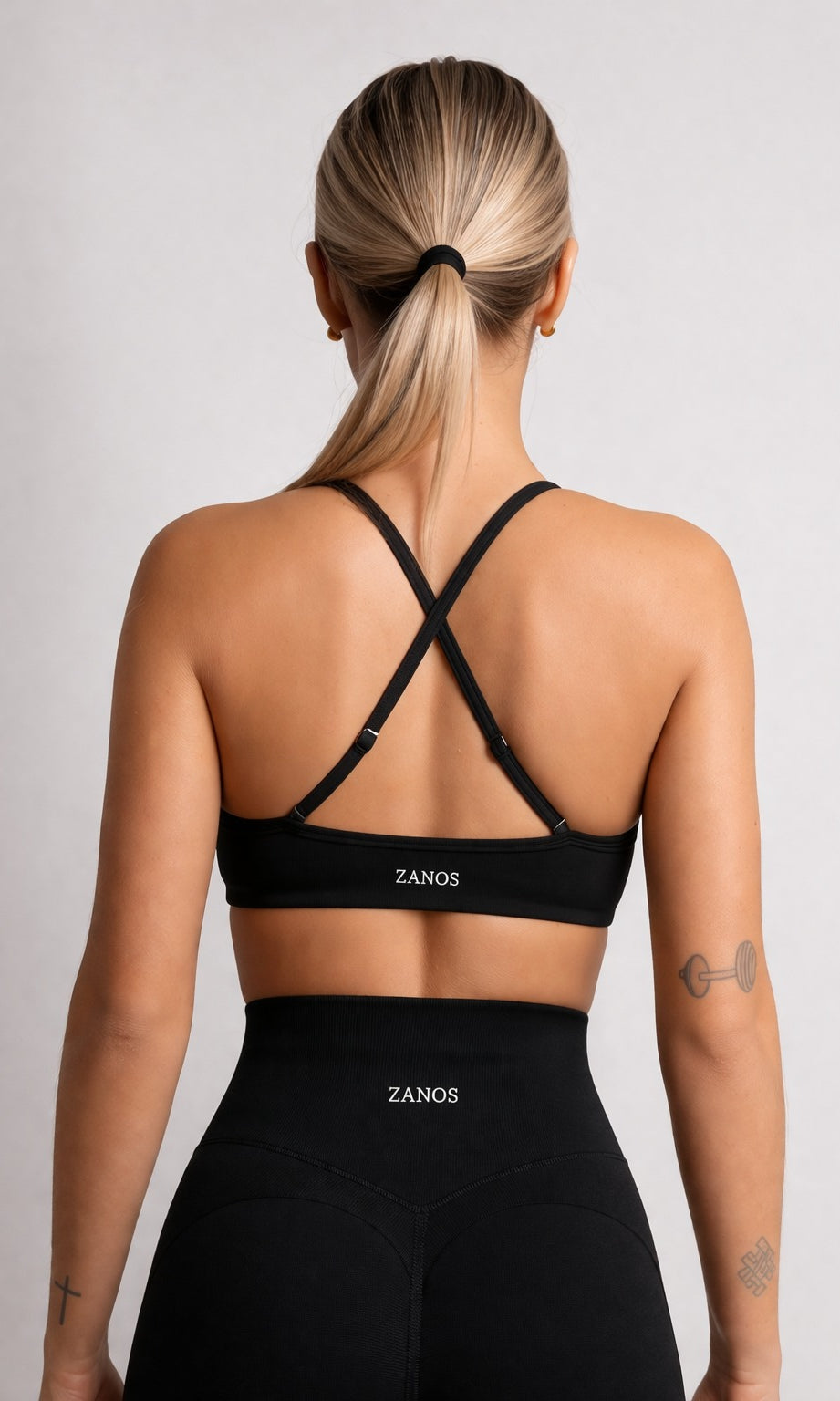 Person wearing a black sports bra and leggings with 'ZANOS' branding on a light gray background