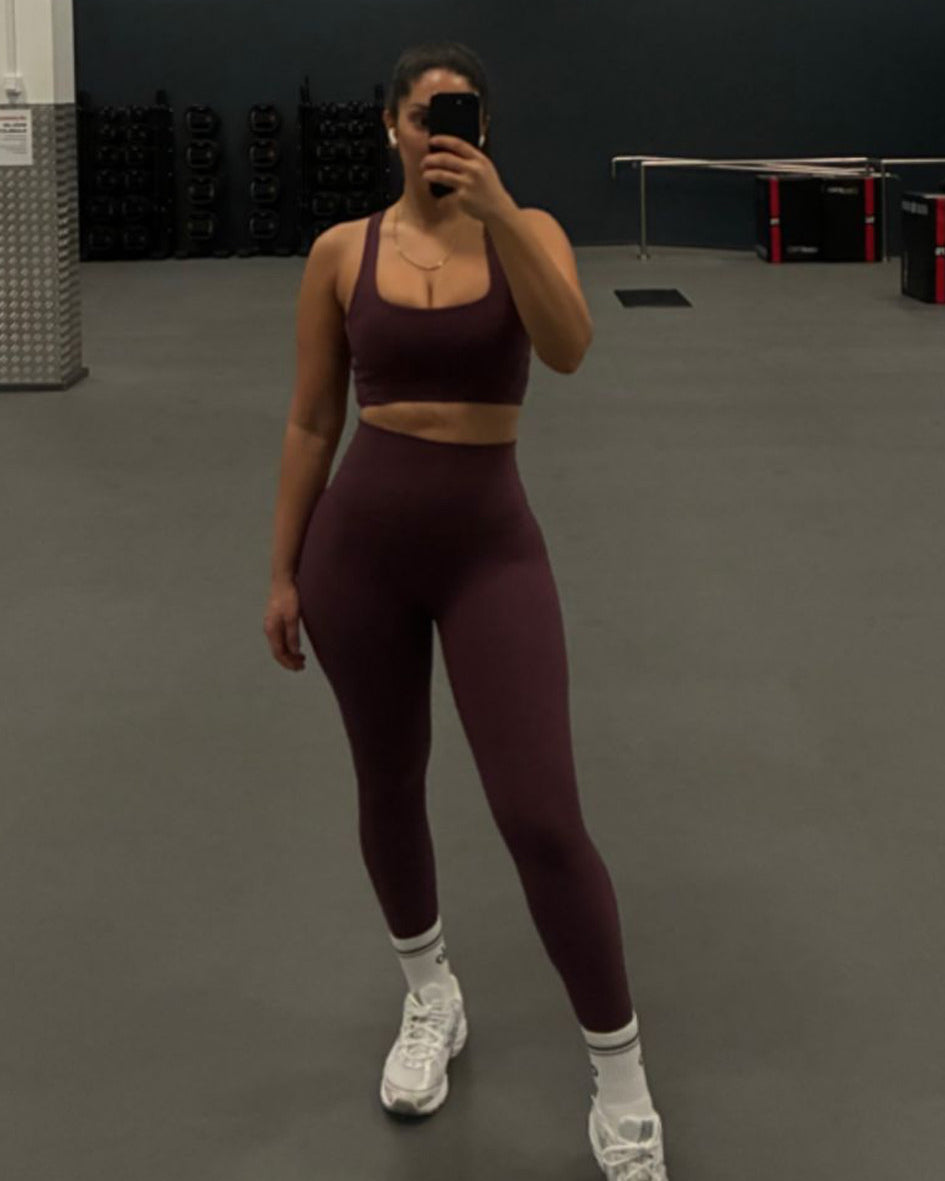 Person taking a mirror selfie wearing a maroon athletic outfit in a gym.
