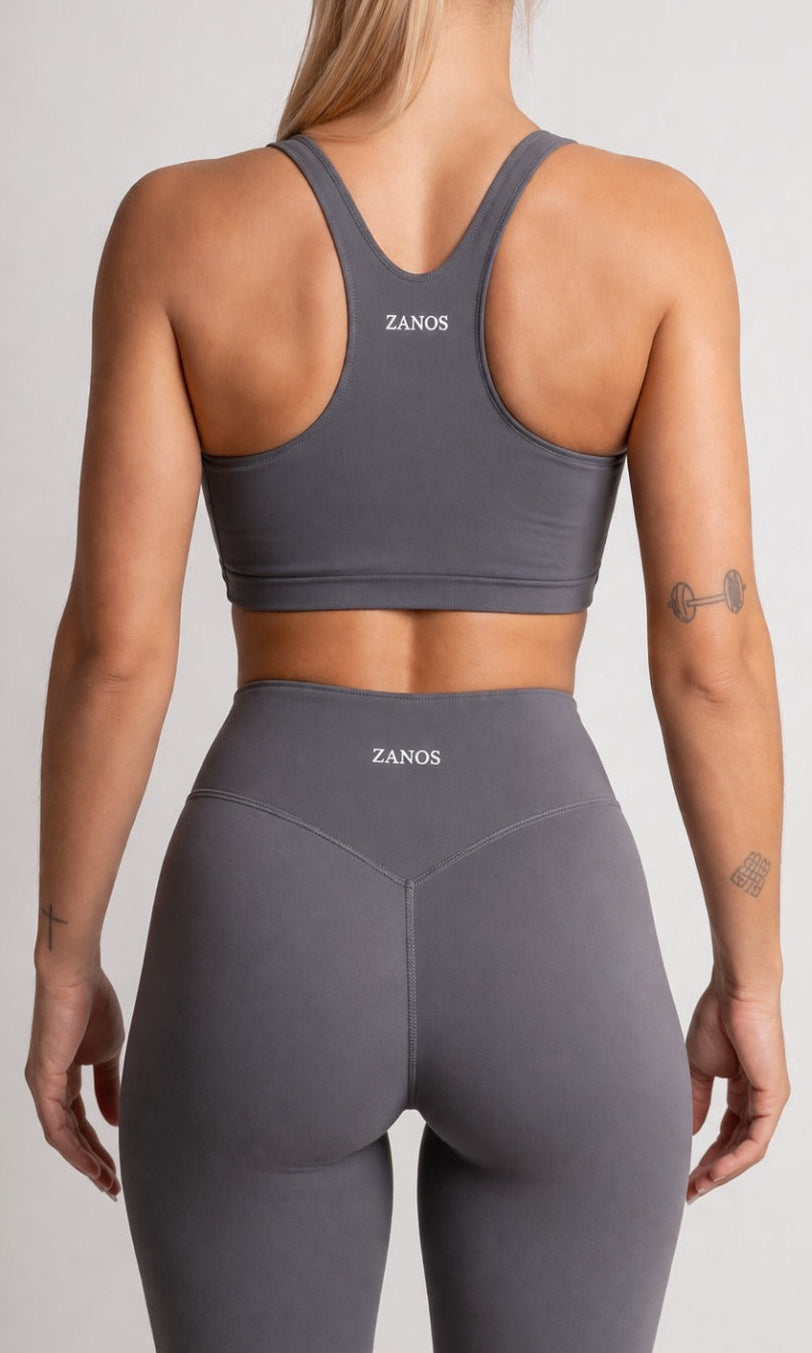 Person wearing a gray sports bra and leggings with 'ZANOS' branding on a light gray background