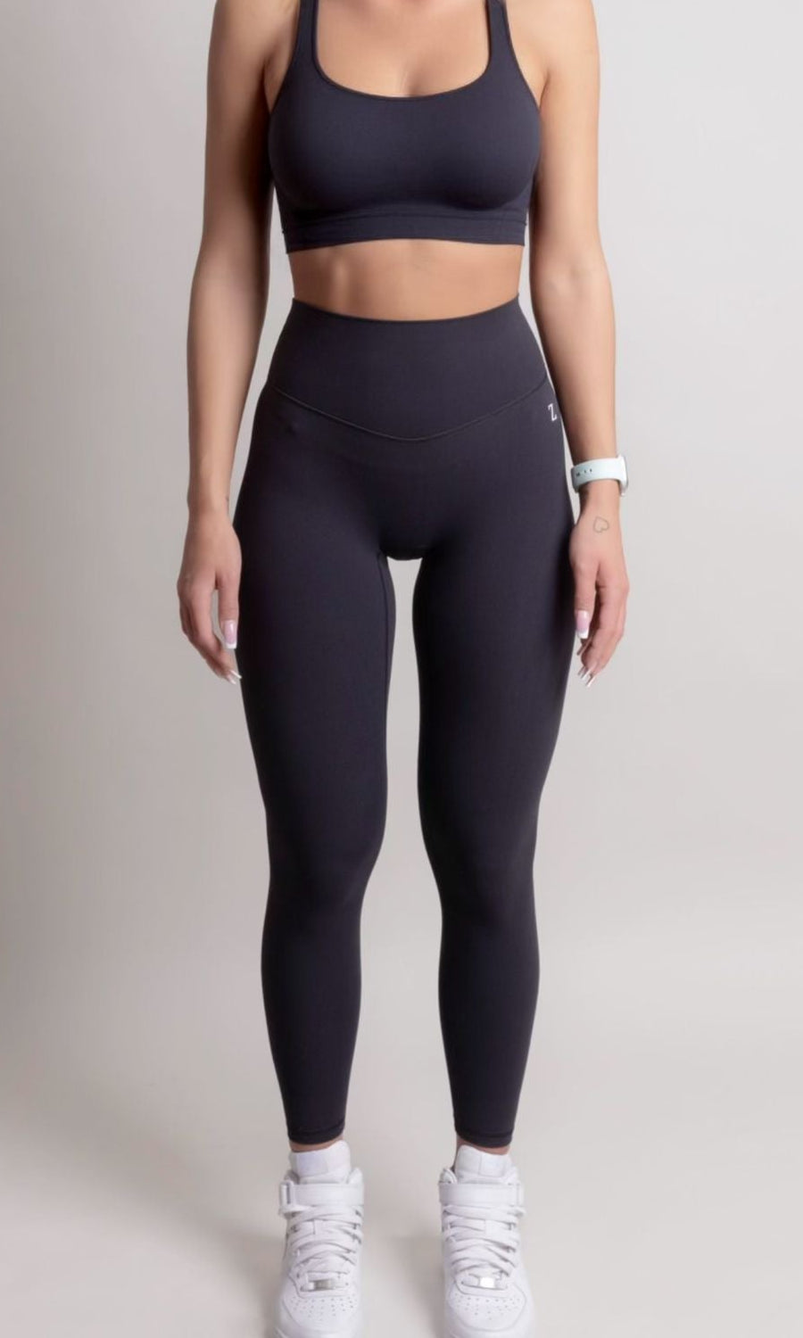 Person wearing black athletic leggings and sports bra on a plain background