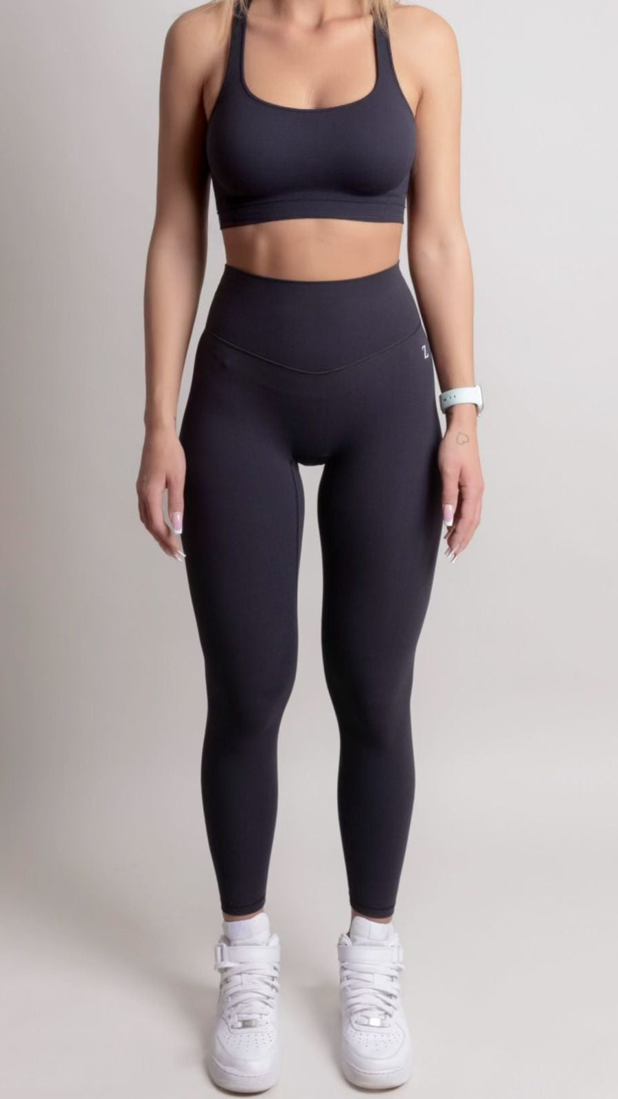 Person wearing black athletic leggings and sports bra on a plain background