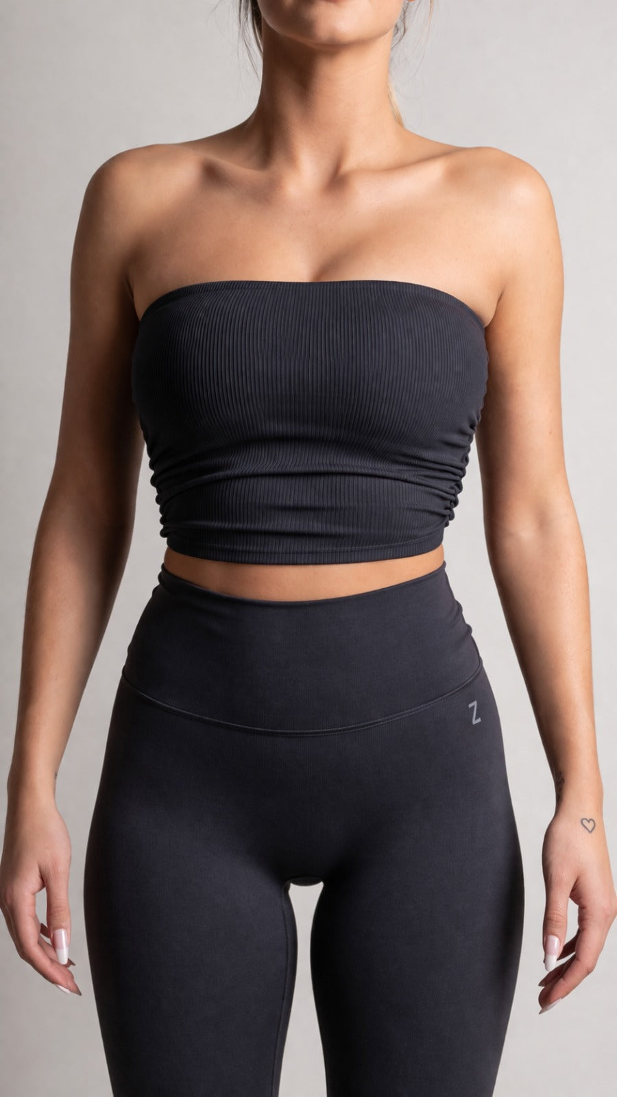 Person wearing a black strapless top and high-waisted leggings on a gray background