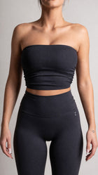 Person wearing a black strapless top and high-waisted leggings on a gray background