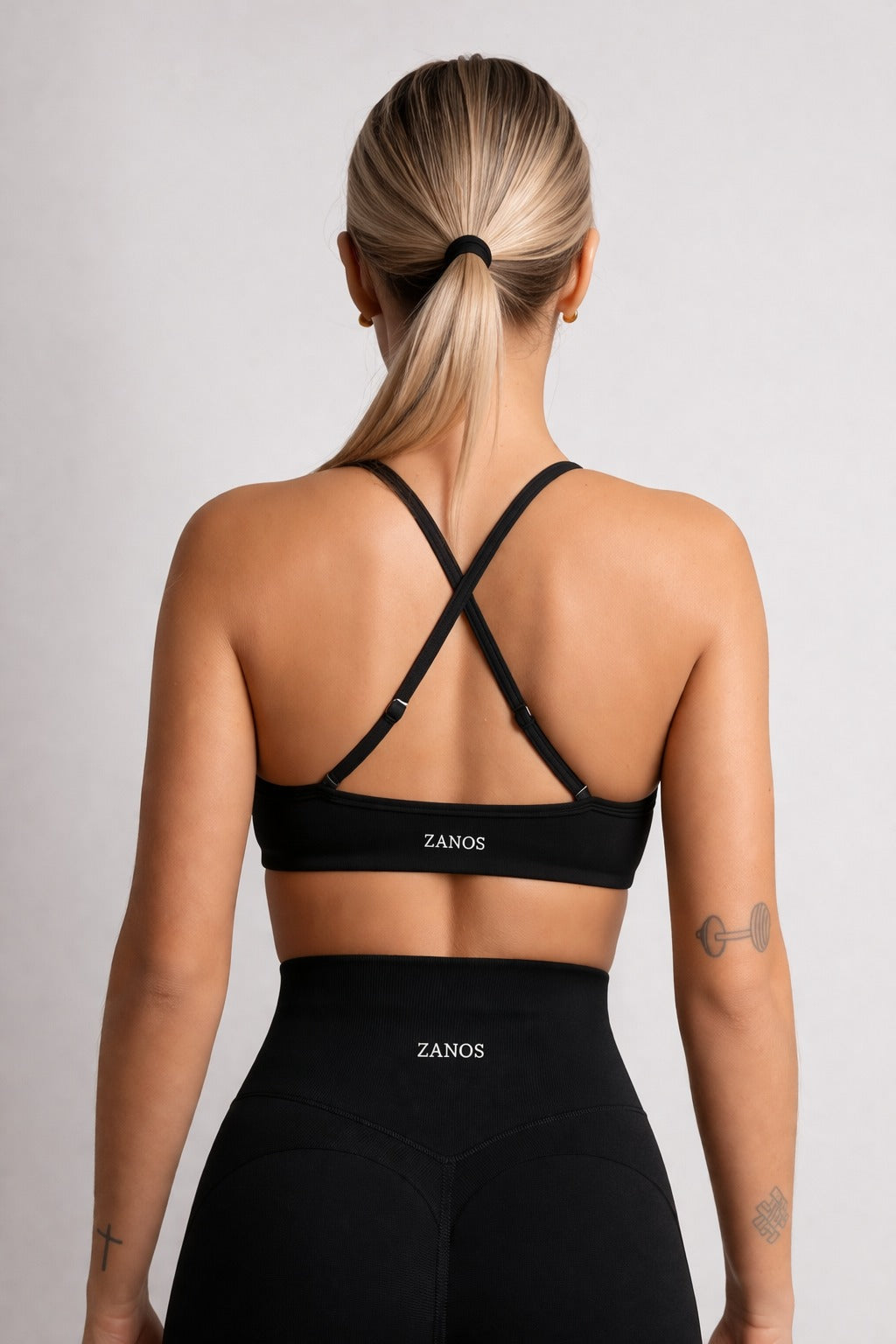 Person wearing a black sports bra and leggings with 'ZANOS' branding on a light gray background
