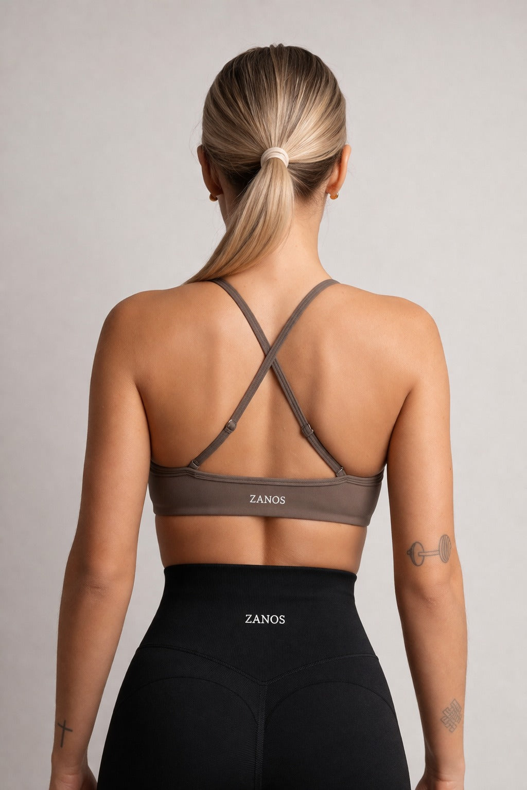 Woman wearing a brown sports bra and black leggings with 'ZANOS' branding on a plain background