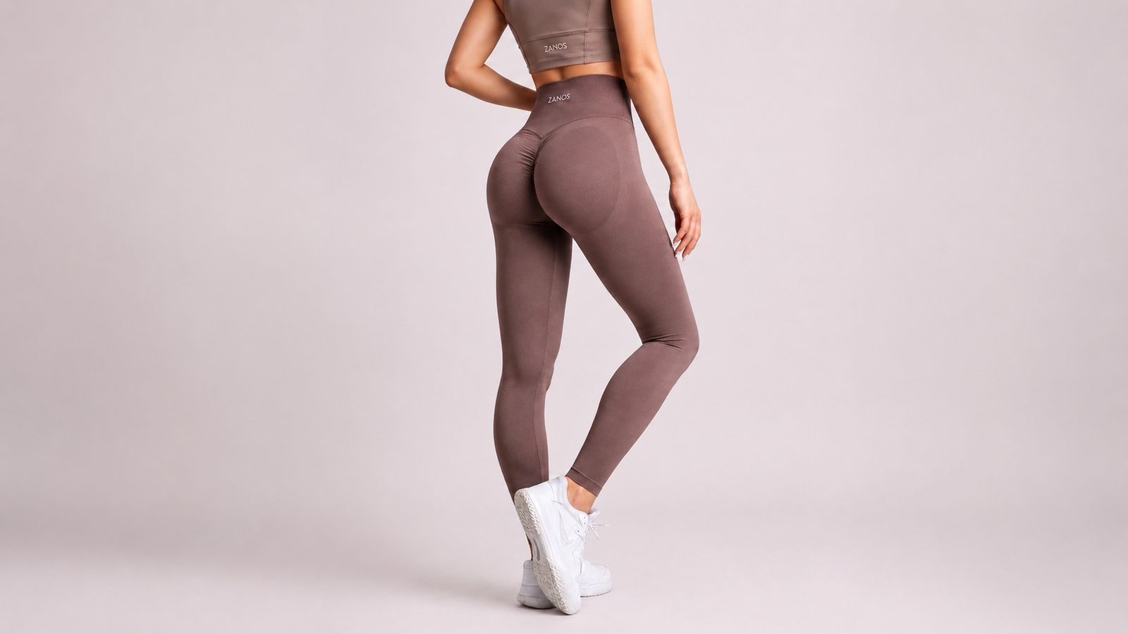 Person wearing brown leggings and a crop top on a light gray background